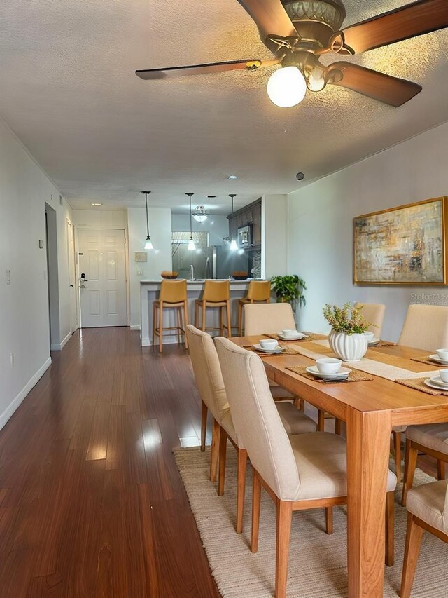 dining space featuring ceiling fan, dark wood-style flooring, baseboards, and a textured ceiling