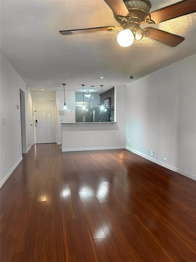unfurnished living room featuring ceiling fan, baseboards, dark wood-style floors, and a textured ceiling