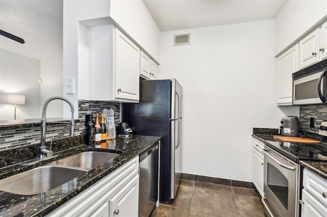 kitchen featuring dark tile floors, sink, dark stone counters, appliances with stainless steel finishes, and backsplash