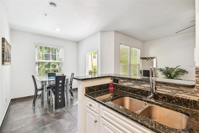 kitchen featuring dark stone counters, white cabinetry, backsplash, dark tile floors, and sink