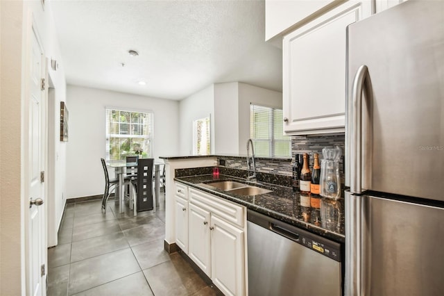 kitchen featuring appliances with stainless steel finishes, sink, white cabinets, dark stone counters, and dark tile flooring