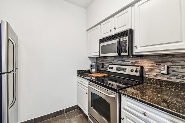 kitchen featuring dark stone counters, appliances with stainless steel finishes, dark tile flooring, white cabinets, and backsplash