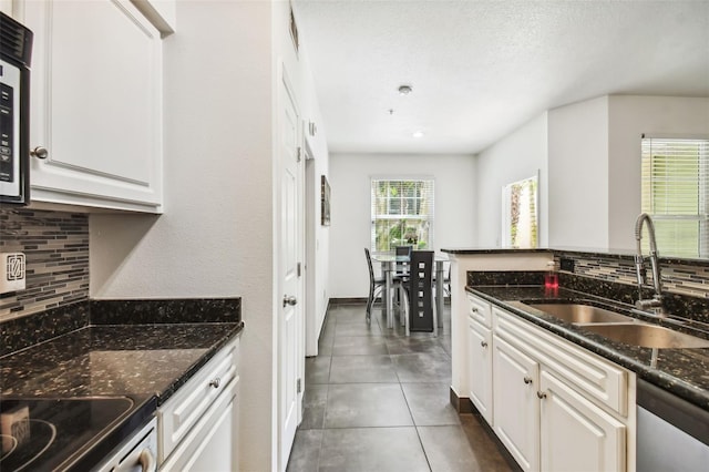 kitchen with white cabinets, dark stone counters, dark tile flooring, and sink