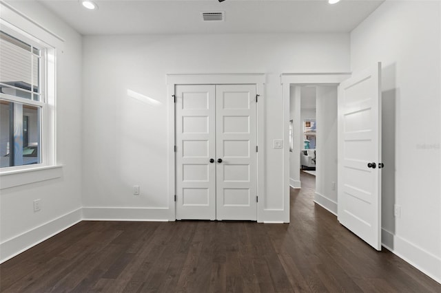 unfurnished bedroom featuring multiple windows, dark hardwood / wood-style floors, and a closet