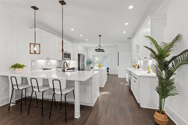 kitchen featuring white cabinetry, sink, stainless steel appliances, kitchen peninsula, and decorative light fixtures