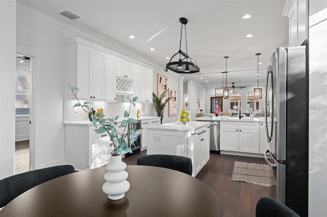 kitchen with kitchen peninsula, stainless steel appliances, dark wood-type flooring, white cabinetry, and a kitchen island