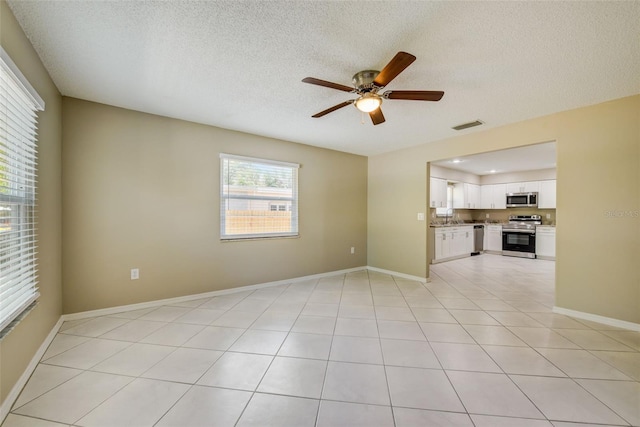 spare room with sink, ceiling fan, light tile floors, and a textured ceiling