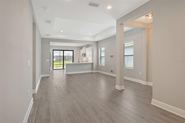 unfurnished living room featuring hardwood / wood-style floors, a tray ceiling, and sink