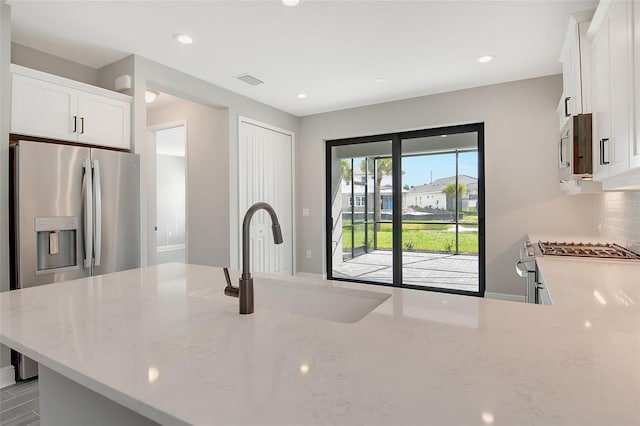 kitchen with decorative backsplash, light stone countertops, white cabinetry, and sink