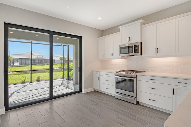 kitchen featuring backsplash, appliances with stainless steel finishes, white cabinetry, and light hardwood / wood-style flooring