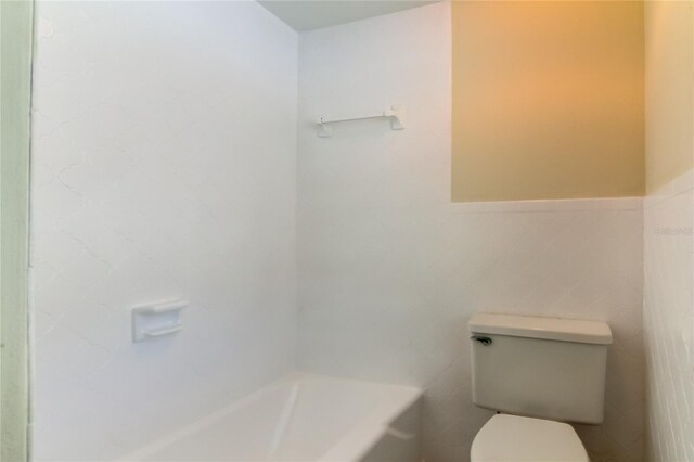 bathroom featuring a bathing tub, toilet, and tile walls