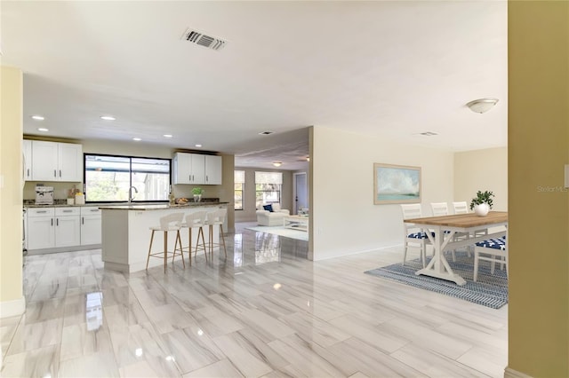 kitchen with a kitchen breakfast bar, white cabinetry, a center island, and sink