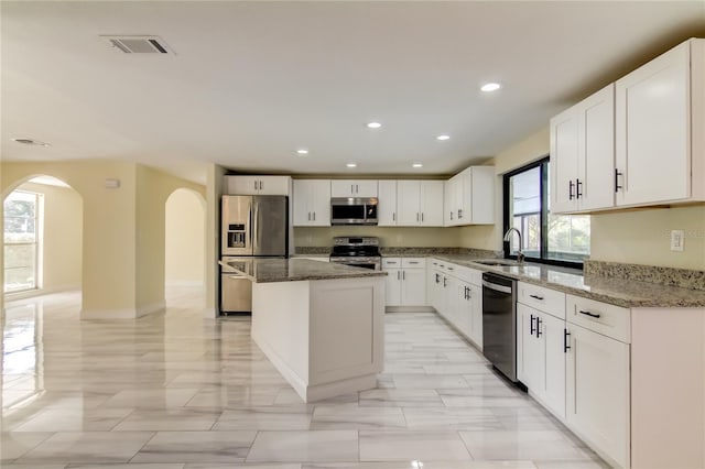 kitchen featuring stainless steel appliances, sink, dark stone countertops, white cabinets, and a kitchen island