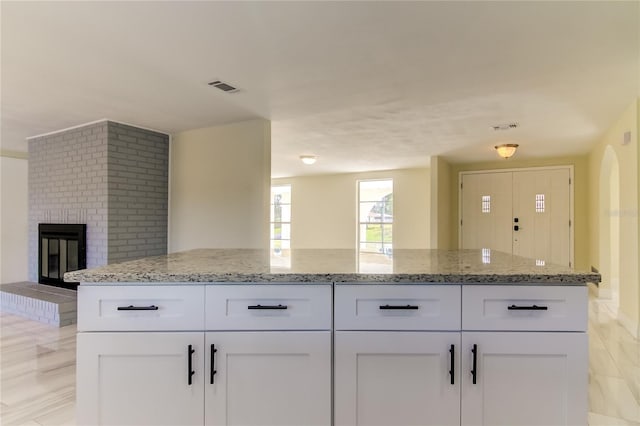 kitchen featuring white cabinets, light stone counters, and a fireplace