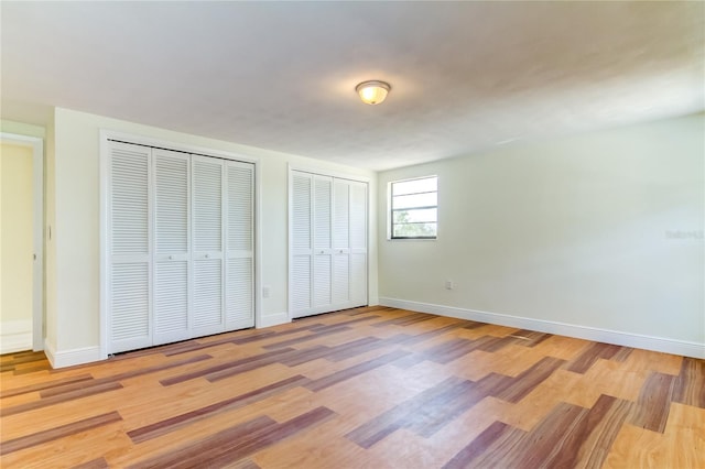 unfurnished bedroom featuring multiple closets and light hardwood / wood-style flooring