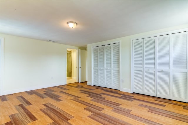 unfurnished bedroom with light wood-type flooring and two closets