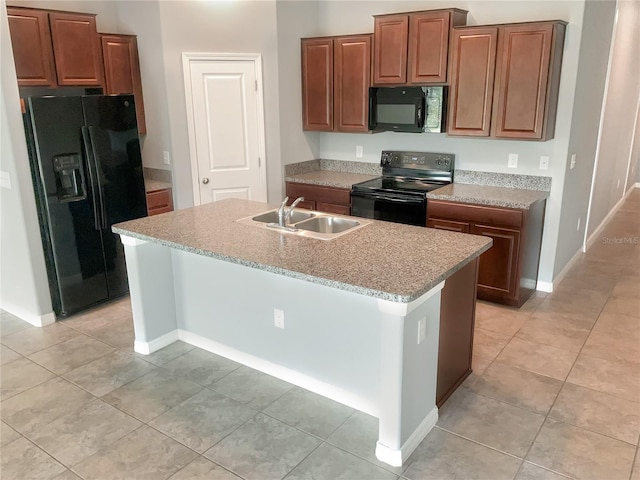 kitchen featuring sink, light tile patterned floors, light stone counters, black appliances, and an island with sink