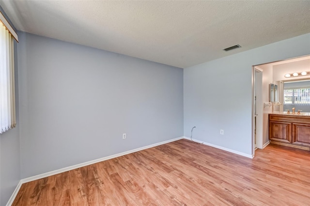 interior space with a textured ceiling, light wood-type flooring, ensuite bath, and sink