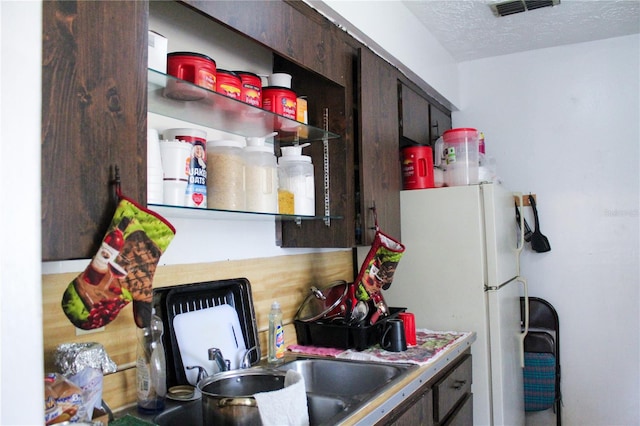 kitchen featuring dark brown cabinets, a textured ceiling, and white fridge