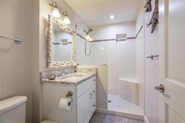 bathroom featuring toilet, a tile shower, and vanity