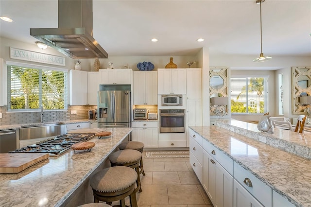 kitchen featuring appliances with stainless steel finishes, island range hood, light tile patterned floors, white cabinetry, and hanging light fixtures