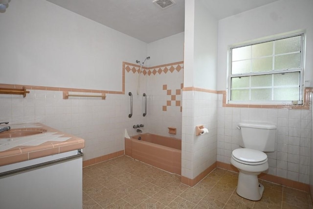 full bathroom with toilet, tiled shower / bath combo, vanity, and tile walls