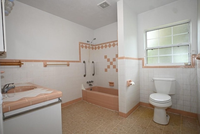 full bathroom with tile walls, toilet, vanity, and tiled shower / bath