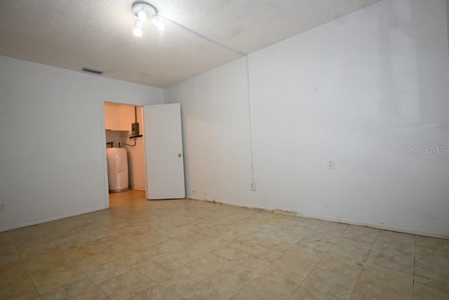 unfurnished room featuring water heater, a textured ceiling, and light tile floors