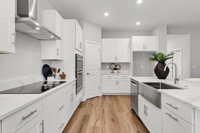 kitchen featuring appliances with stainless steel finishes, sink, white cabinets, light stone countertops, and wall chimney range hood