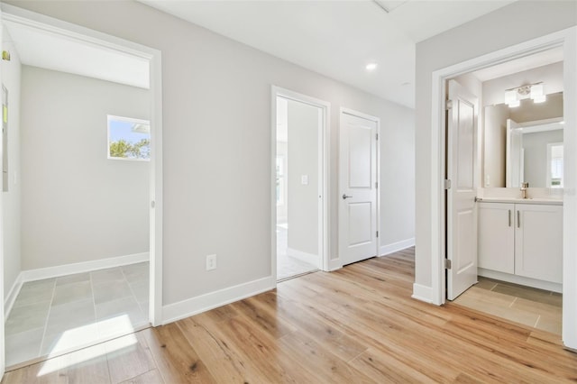 unfurnished bedroom featuring ensuite bathroom, sink, and light hardwood / wood-style flooring