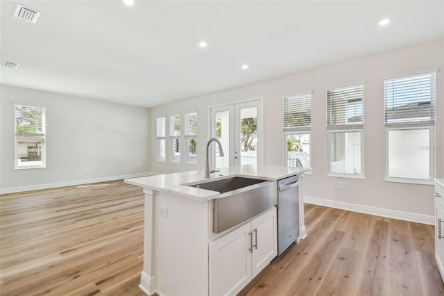 kitchen with white cabinets, french doors, an island with sink, sink, and stainless steel dishwasher