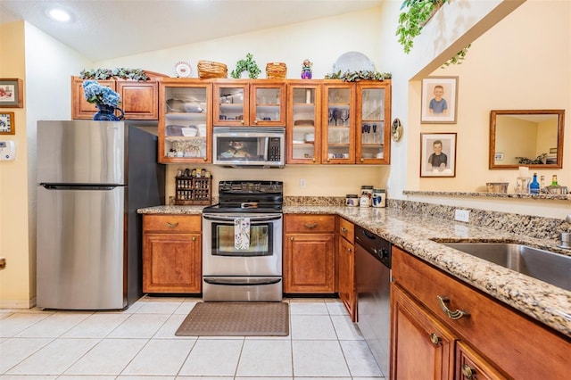 kitchen featuring light tile floors, light stone countertops, vaulted ceiling, and stainless steel appliances