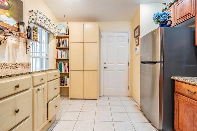 kitchen featuring light tile floors, light stone countertops, and stainless steel refrigerator