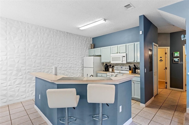 kitchen with a kitchen breakfast bar, a center island, light tile flooring, a textured ceiling, and white appliances