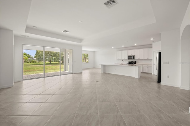 unfurnished living room with light tile flooring, a healthy amount of sunlight, and a raised ceiling