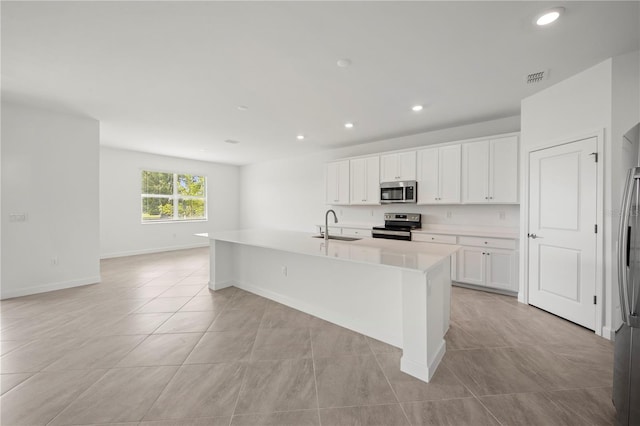 kitchen with light tile flooring, a center island with sink, stainless steel appliances, and white cabinetry