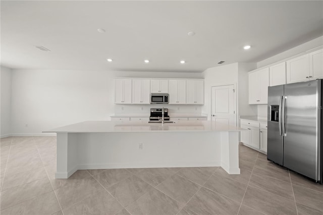 kitchen with an island with sink, stainless steel appliances, light tile flooring, and white cabinets