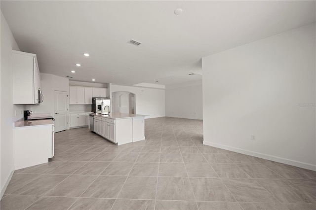 kitchen with a center island with sink, white cabinetry, range, and light tile flooring