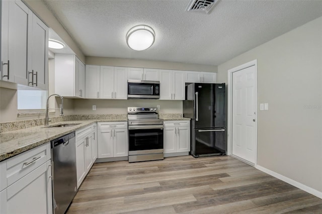 kitchen with sink, white cabinets, light hardwood / wood-style flooring, stainless steel appliances, and a textured ceiling