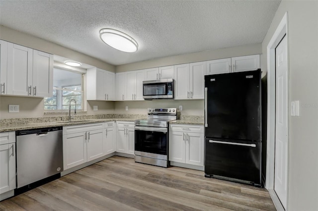 kitchen with appliances with stainless steel finishes, white cabinetry, sink, and light wood-type flooring