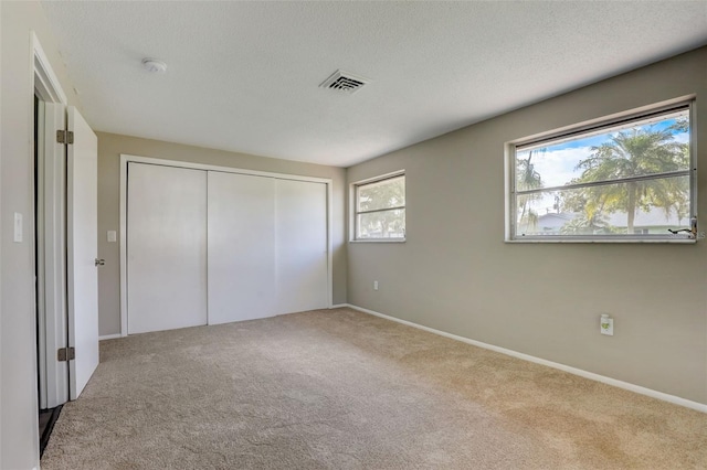 unfurnished bedroom with a closet, a textured ceiling, and light colored carpet