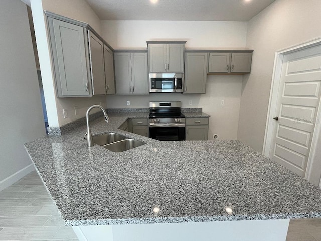 kitchen with gray cabinetry, sink, stainless steel appliances, kitchen peninsula, and dark stone countertops