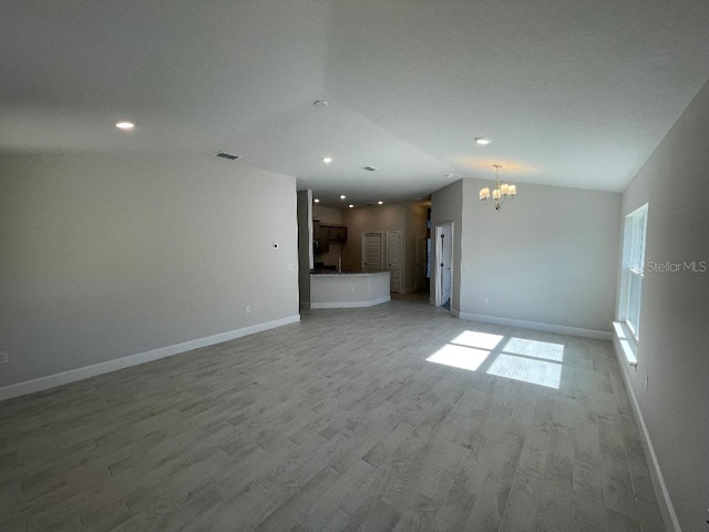 unfurnished living room featuring a notable chandelier, lofted ceiling, and light hardwood / wood-style flooring