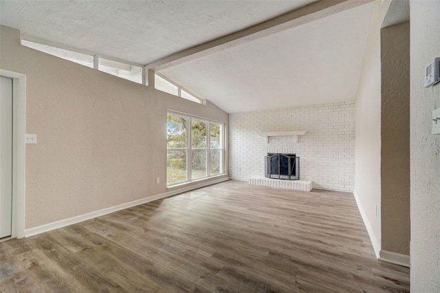 unfurnished living room with hardwood / wood-style flooring, lofted ceiling with beams, a brick fireplace, and a textured ceiling