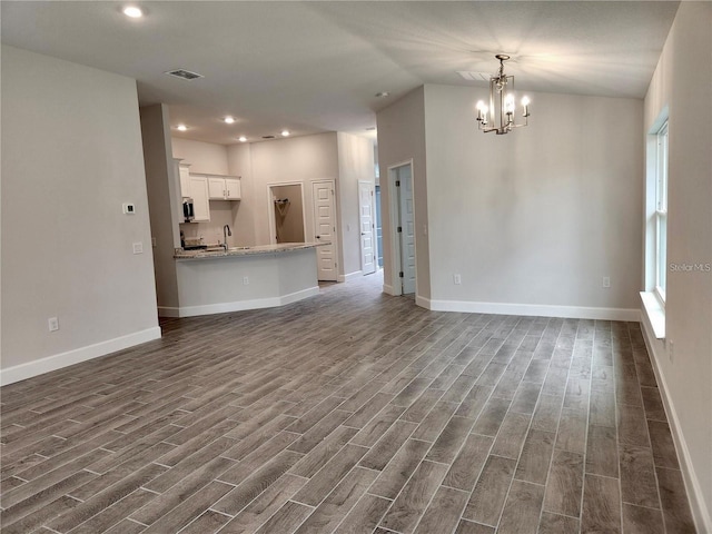 unfurnished living room featuring an inviting chandelier, sink, and dark wood-type flooring