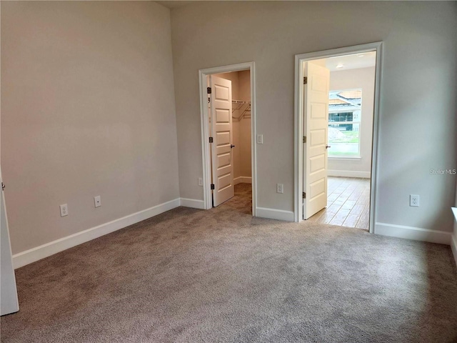 unfurnished bedroom featuring a closet, a walk in closet, and light colored carpet