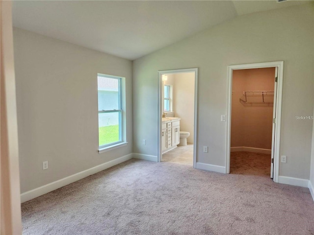 unfurnished bedroom with connected bathroom, a spacious closet, light carpet, a closet, and lofted ceiling