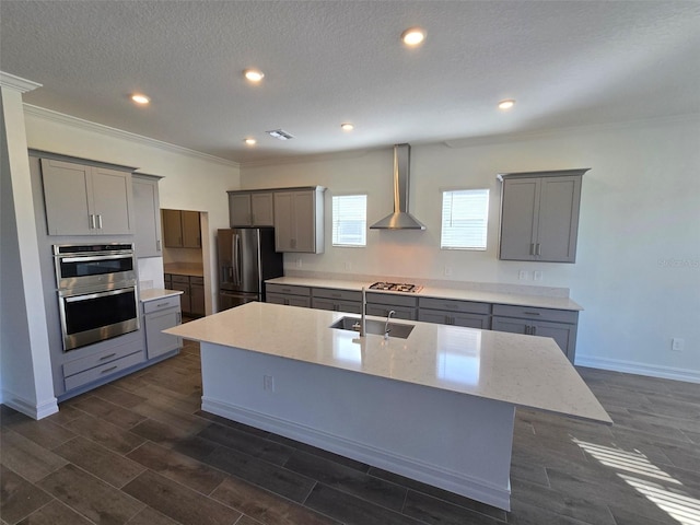 kitchen featuring wall chimney range hood, appliances with stainless steel finishes, sink, dark wood-type flooring, and a center island with sink