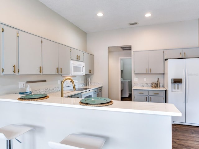 kitchen featuring kitchen peninsula, white appliances, gray cabinets, a breakfast bar area, and dark wood-type flooring