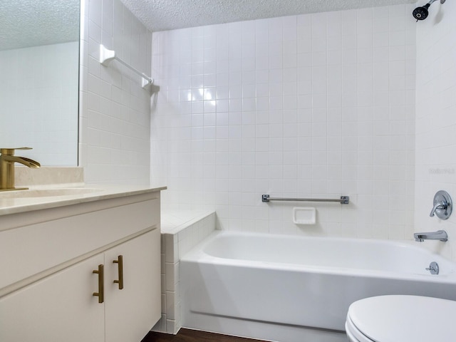 full bathroom with toilet, large vanity, tiled shower / bath combo, and a textured ceiling